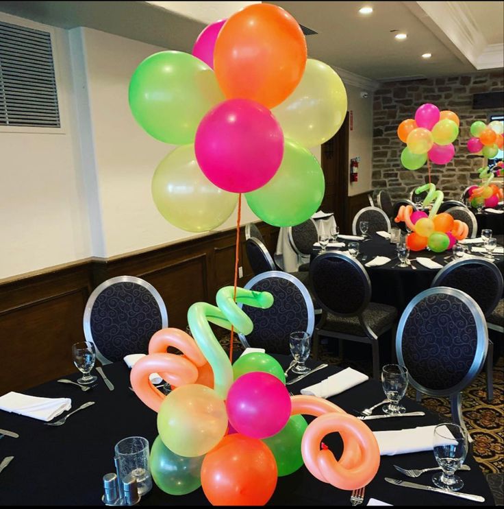 there are many balloons on the table in this room with black tables cloths and chairs