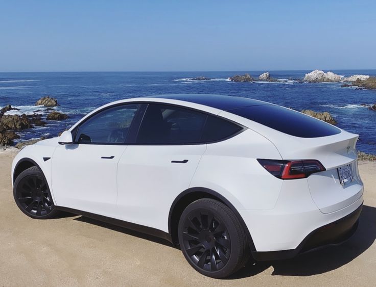 a white car parked on the beach next to the ocean