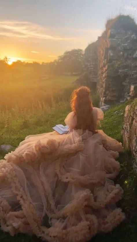 a teddy bear sitting on the grass in front of an old stone wall at sunset