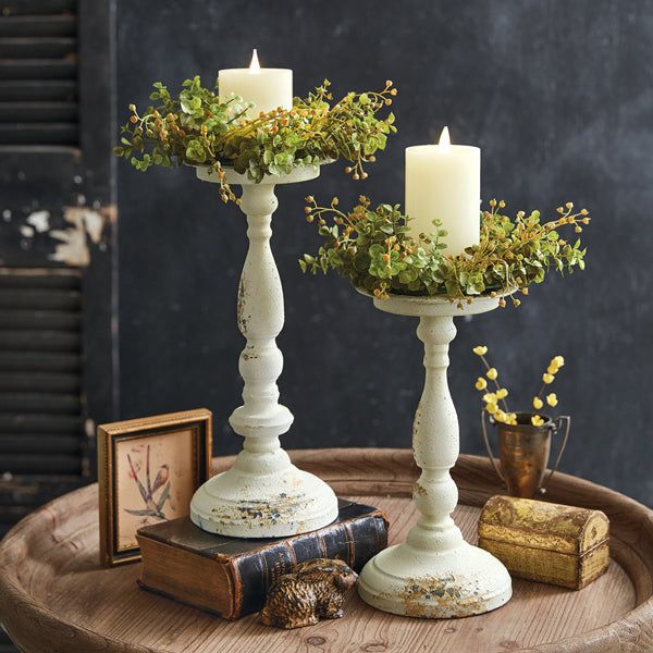 two candles are sitting on a table with books and plants in the vases next to them