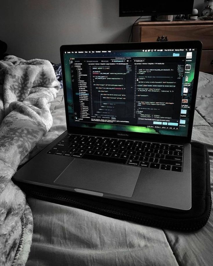 an open laptop computer sitting on top of a bed next to a pillow and blanket