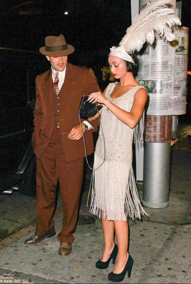 a man in a brown suit and hat standing next to a woman