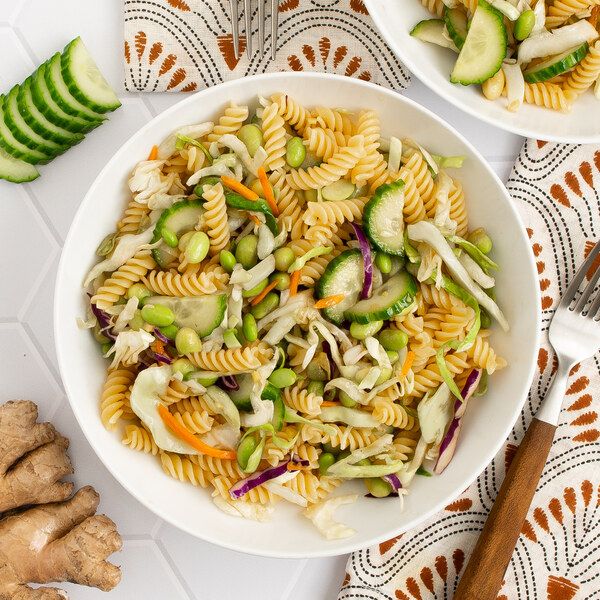 two bowls filled with pasta salad next to sliced cucumbers and slices of celery