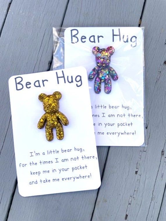 two bear hug brooches are sitting on a wooden table next to each other