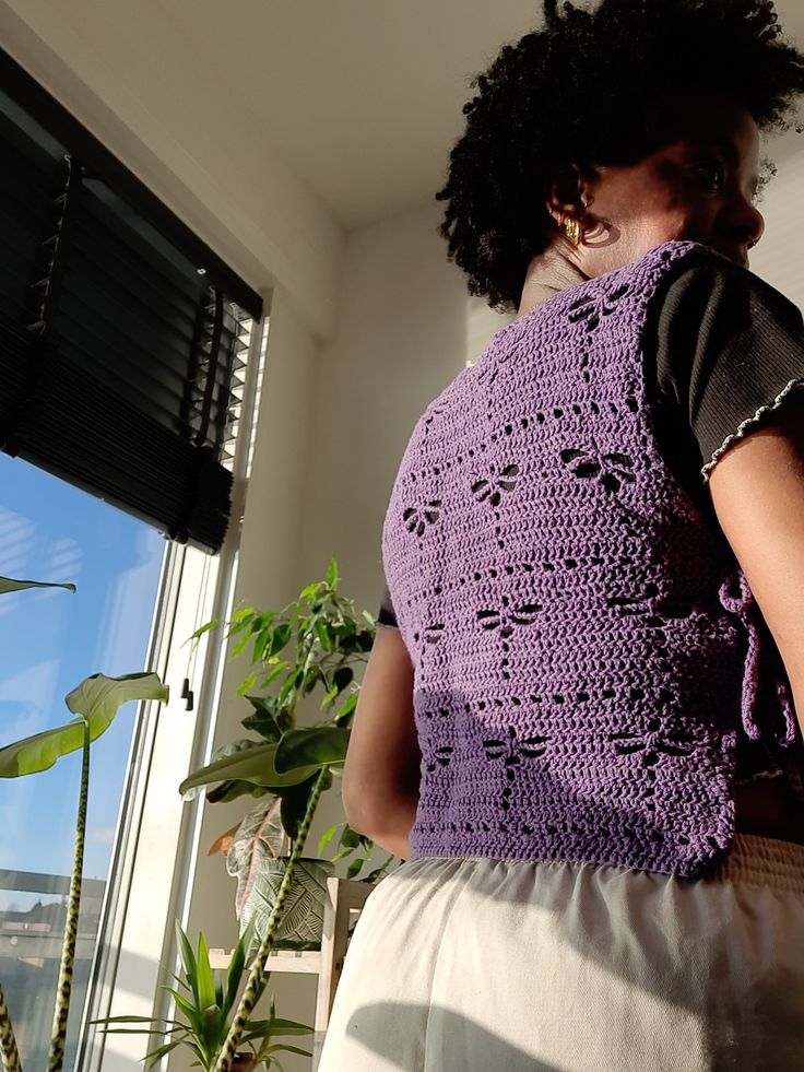 a woman standing in front of a window wearing a purple crochet top