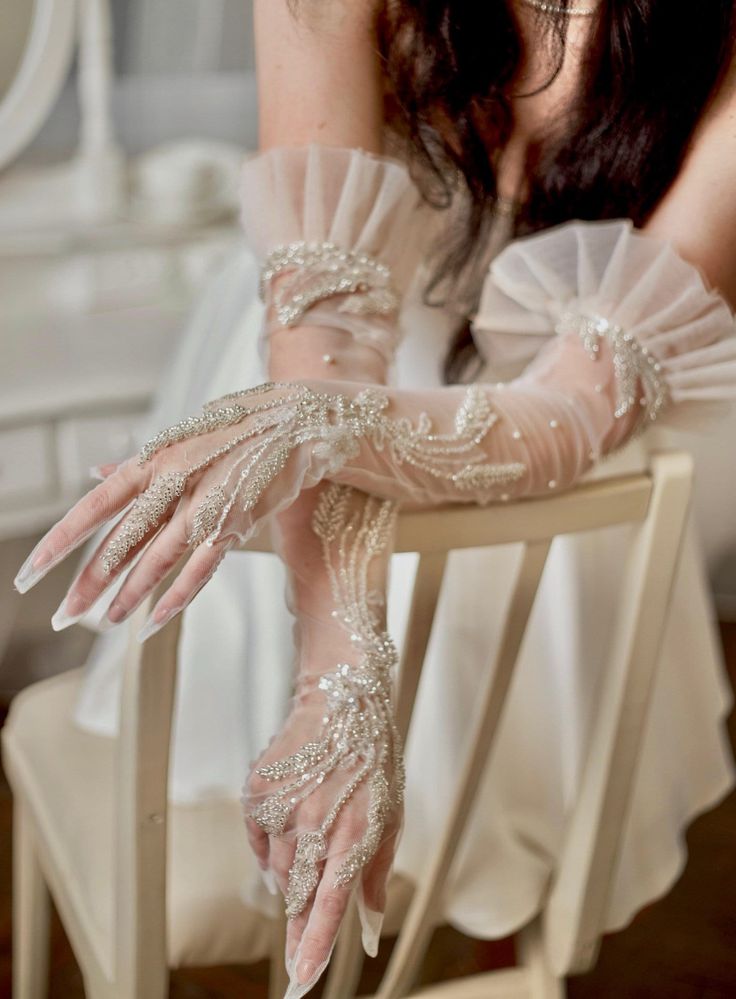 a woman sitting on top of a white chair wearing long gloves and holding onto her arm