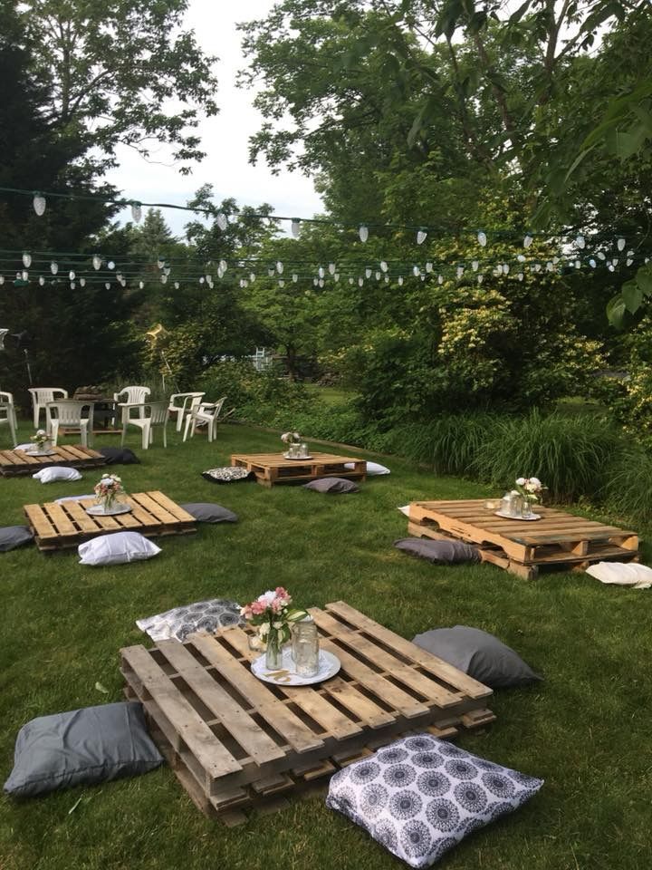 several wooden pallets are set up on the grass for an outdoor party with string lights strung above them