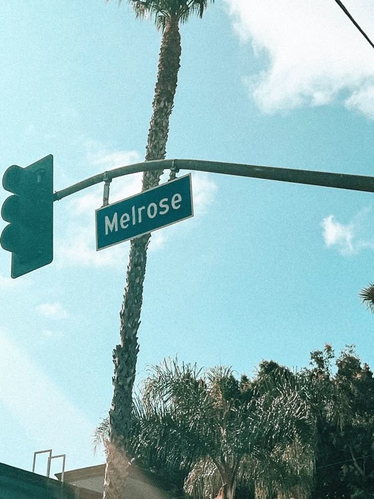 the street sign for melrosee is hanging from a traffic light pole with palm trees in the background