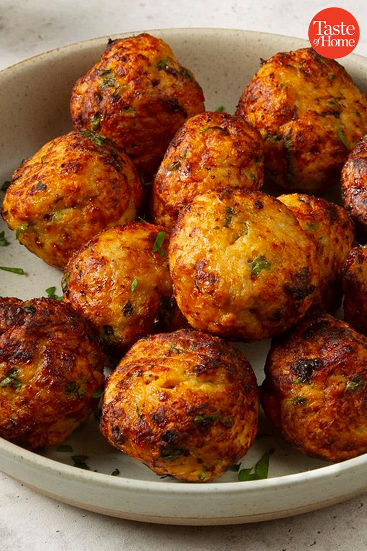 a white bowl filled with cooked meatballs on top of a marble counter next to a knife and fork