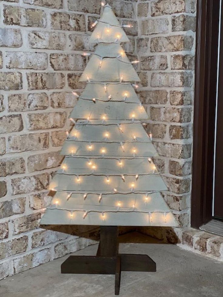 a small white christmas tree with lights on it sitting in front of a brick wall