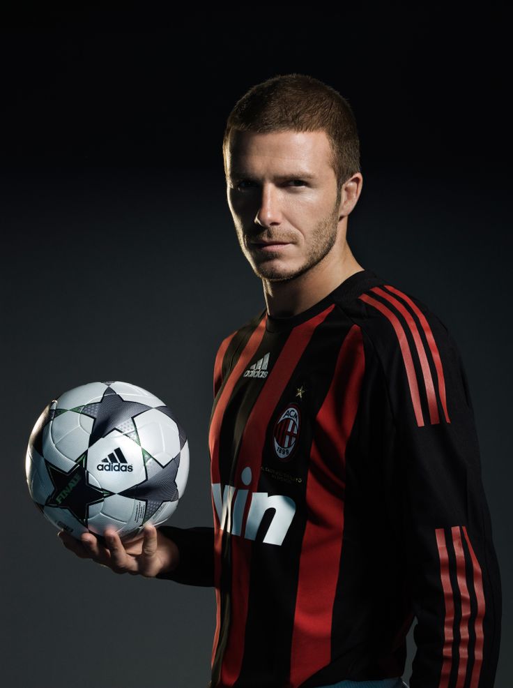 a man is holding a soccer ball in his right hand and posing for the camera