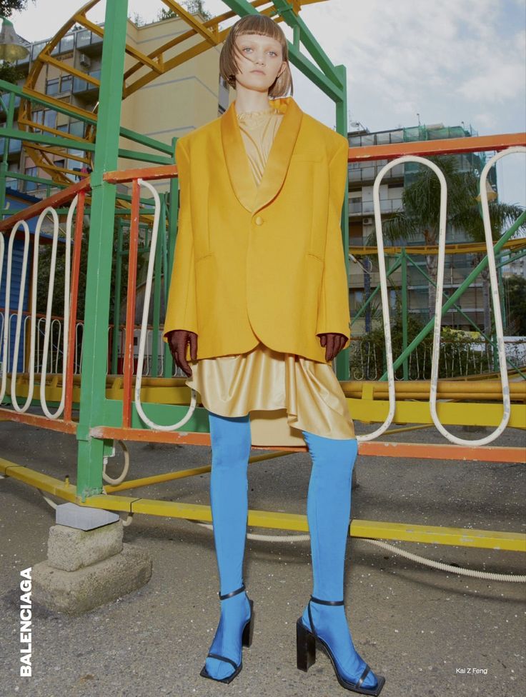 a woman standing in front of a playground with blue tights and yellow blazer