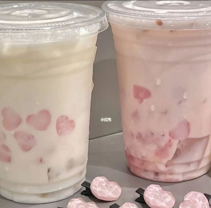 two plastic cups filled with ice cream and pink heart shaped candies next to each other