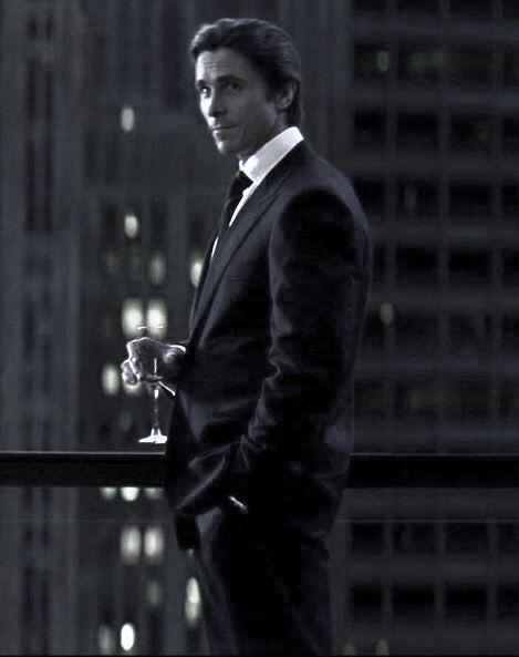 a man in a suit and tie holding a wine glass looking off into the distance