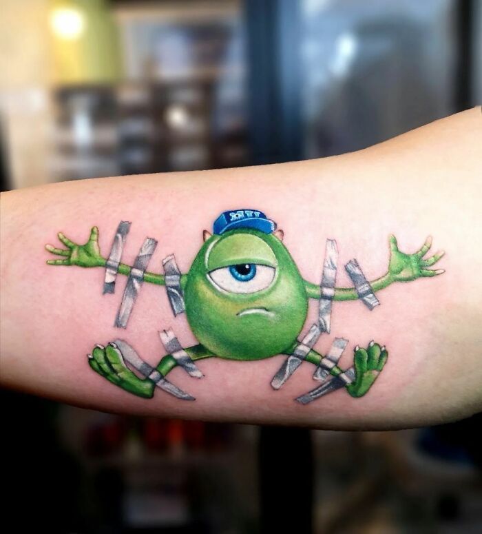 a green frog tattoo on the arm with barbed wire around it's legs and eyes