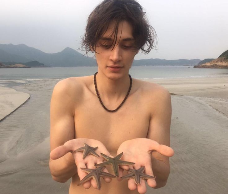 a shirtless young man holding two starfishs in his hands on the beach