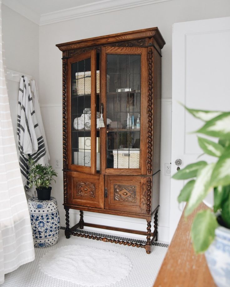 an old china cabinet with glass doors in a white and blue room next to a potted plant