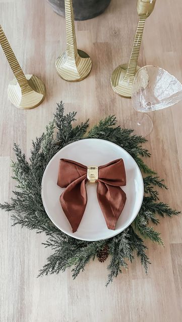 a white plate topped with a brown bow on top of a wooden table next to two gold candles