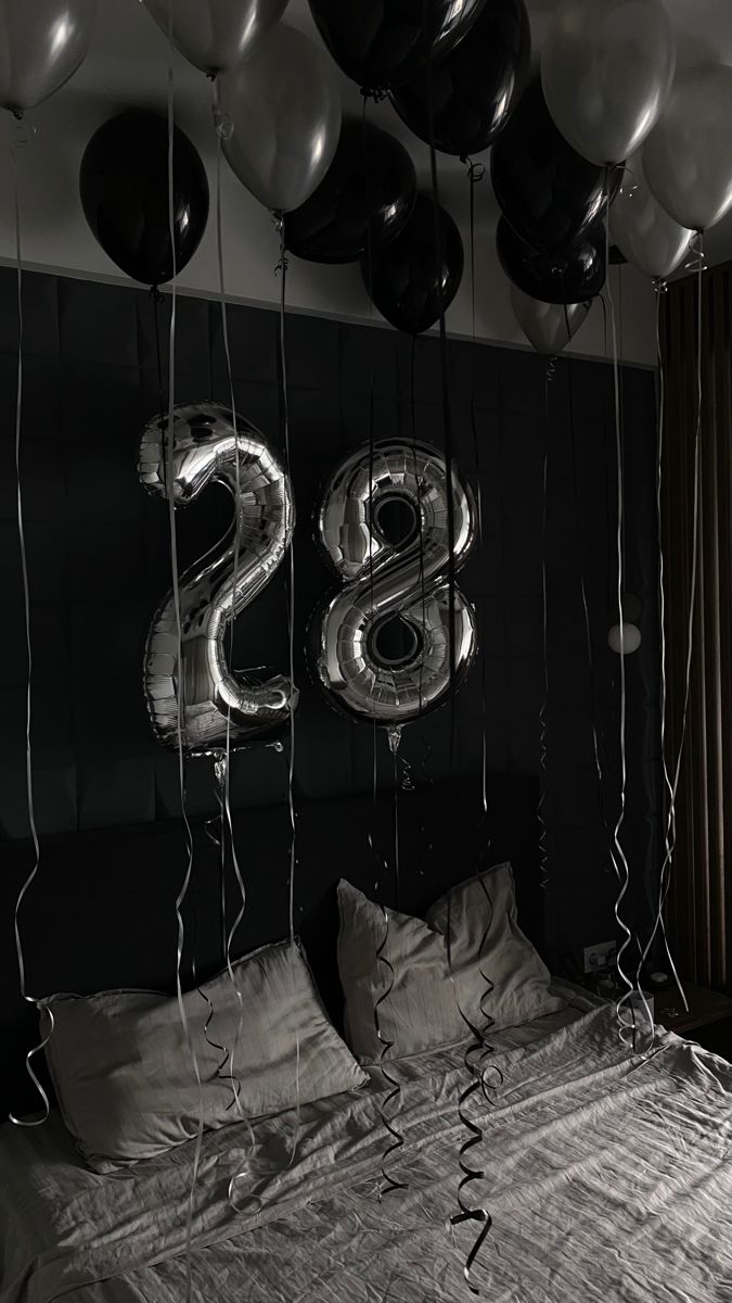 black and white photograph of balloons hanging from the ceiling above a bed with an overstuffed cover