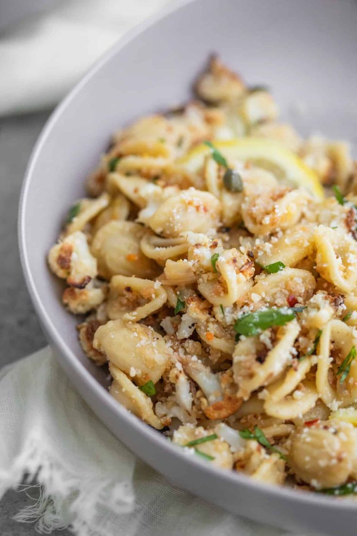 a white bowl filled with pasta covered in cheese and herbs on top of a table