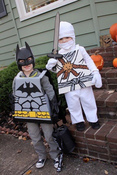 two children dressed up as batman and catwoman standing next to each other in front of a house