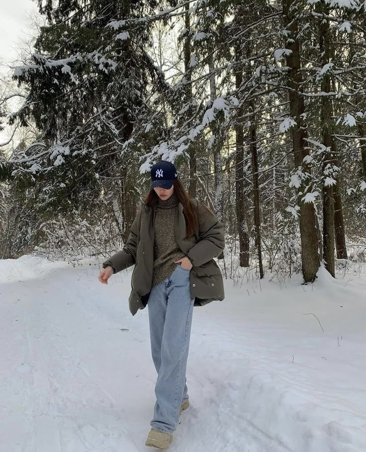 a woman is walking through the snow in front of some trees