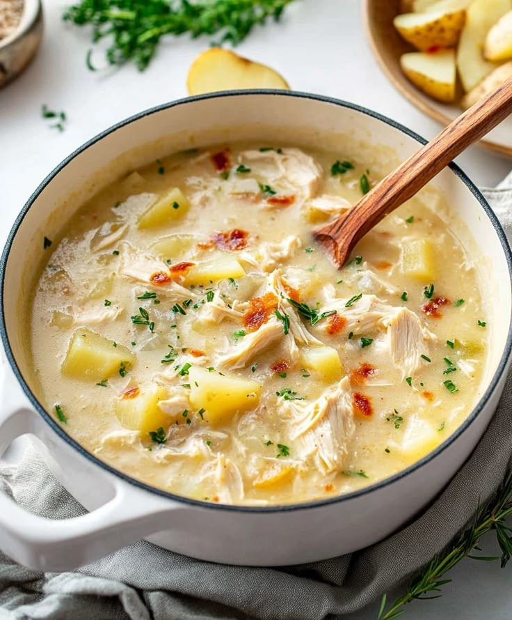 a bowl of chicken and potato soup with a wooden spoon in it on a white surface