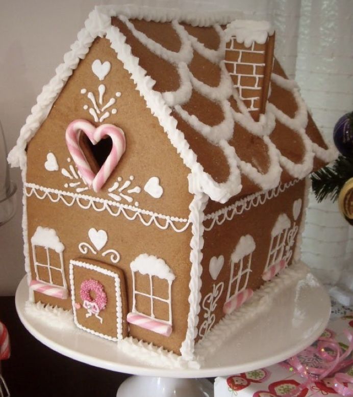 a gingerbread house decorated with icing and pink decorations on a cake platter