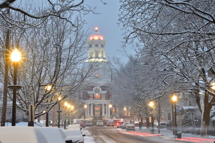 a snowy street with cars parked on the side and a clock tower in the background