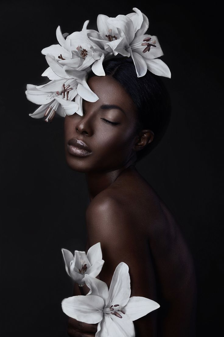 a woman with white flowers on her head and black skin, in front of a dark background