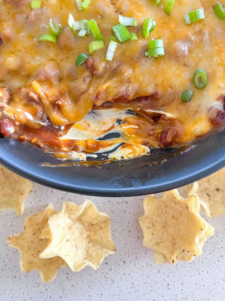 an enchilada with meat, cheese and green onions in a black plate