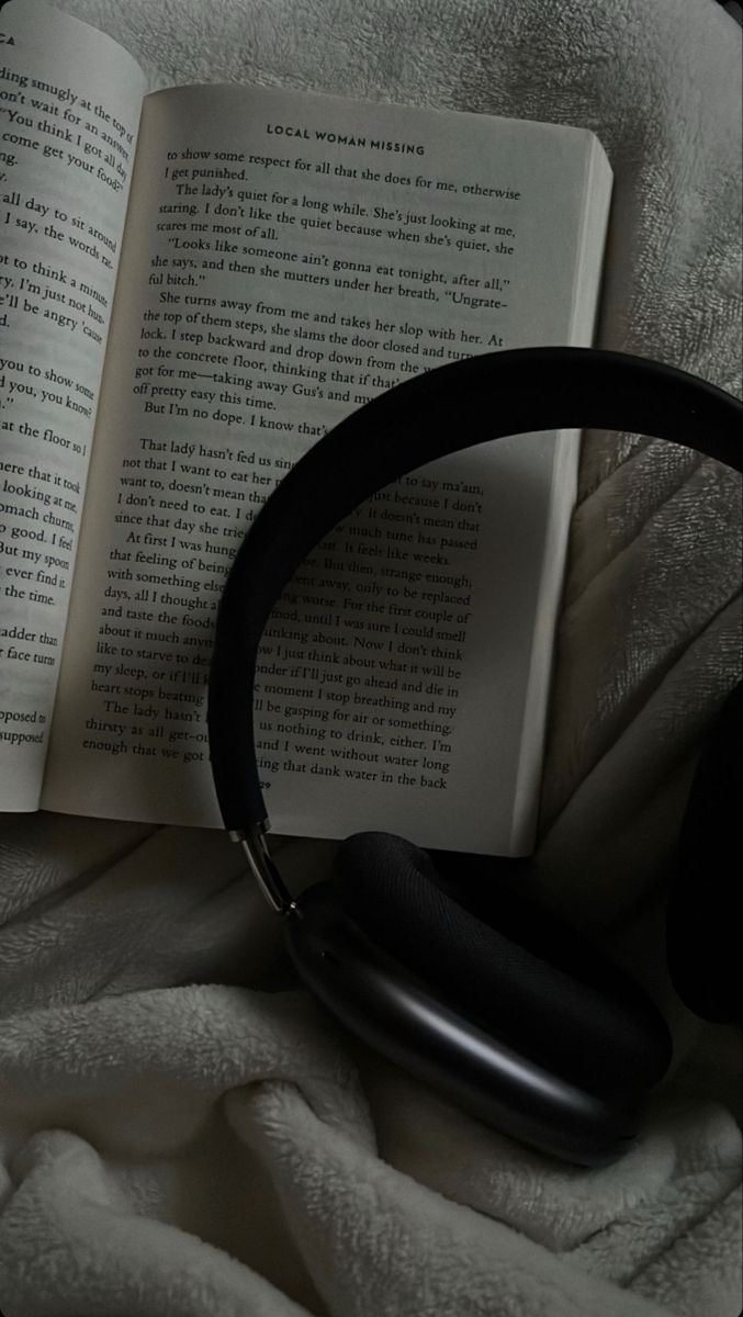 an open book sitting on top of a bed next to headphones