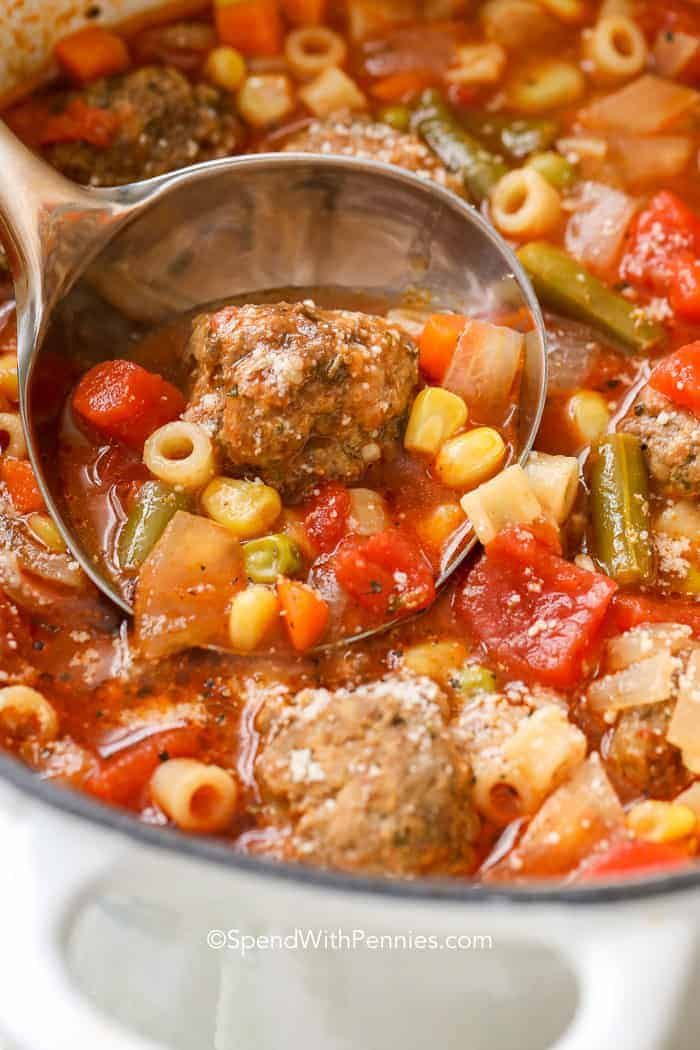 a ladle full of meatballs and pasta soup