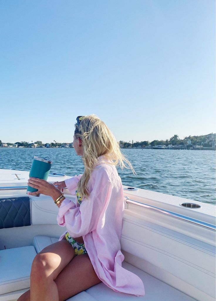 a woman sitting on the back of a boat holding a cup in her hand and looking out over the water