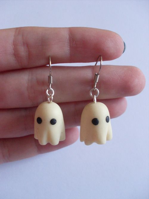 a pair of white ghost earrings with black eyes hanging from silver earwires on a person's hand