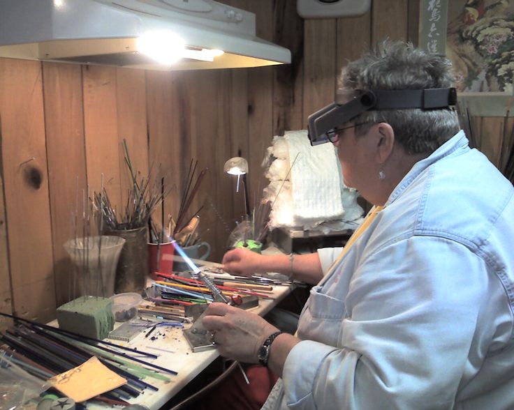 an older woman sitting at a table working on some art work in front of her