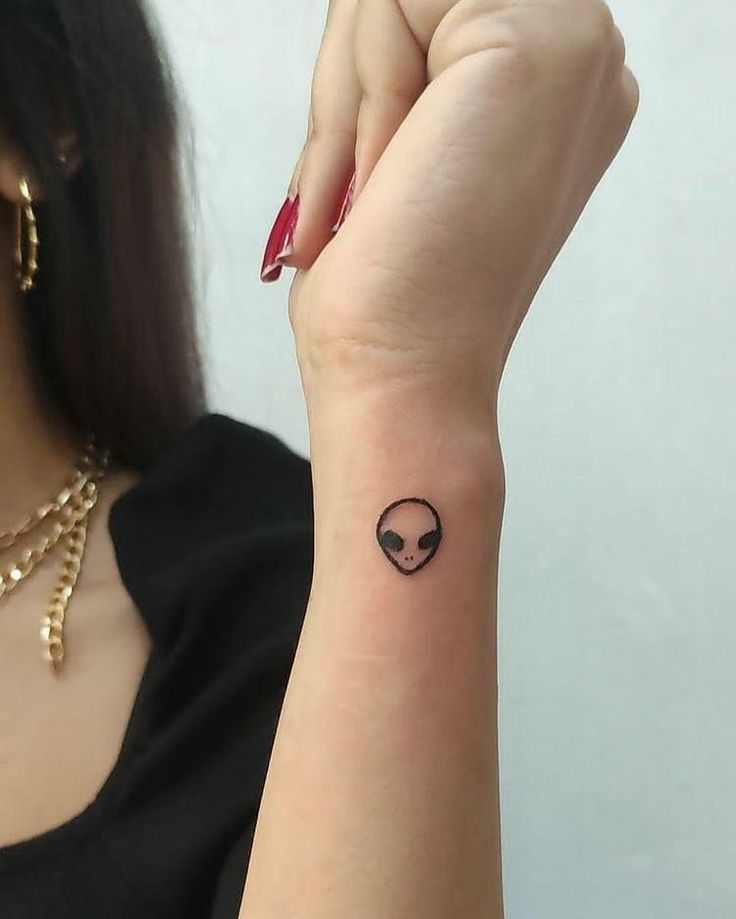 a woman's arm with a small tattoo on the wrist and an alien head