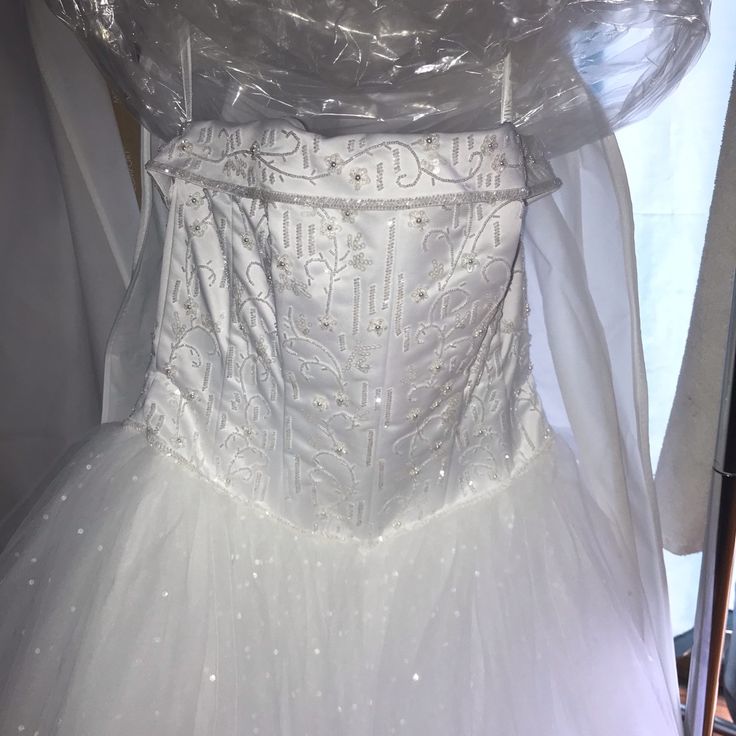 a white wedding dress is on display in a shop window, with plastic covering it's back