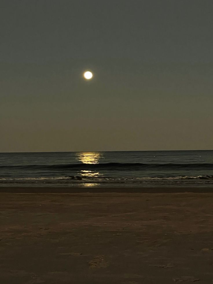 the sun is setting over the ocean and it's reflection in the water on the beach