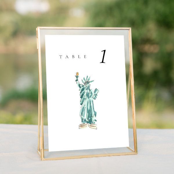 a table number card with the statue of liberty in watercolor on white paper and gold frame