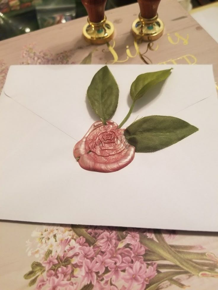 an envelope with a rose on it and two waxed roses attached to the front