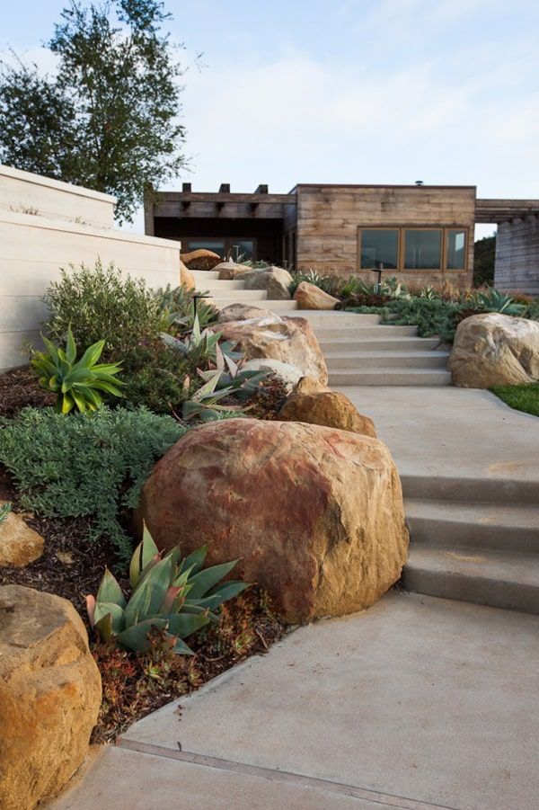 some rocks and plants in front of a house with stairs leading up to the entrance