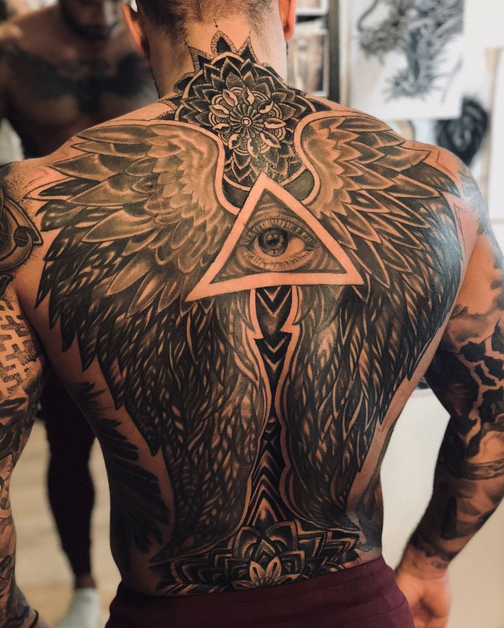 a man with tattoos on his back has an all seeing triangle and wings tattoo on his back