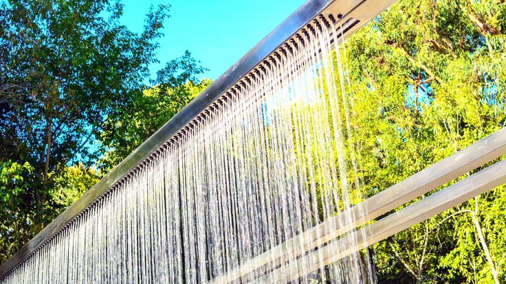 a shower head with water running down it's side and trees in the background