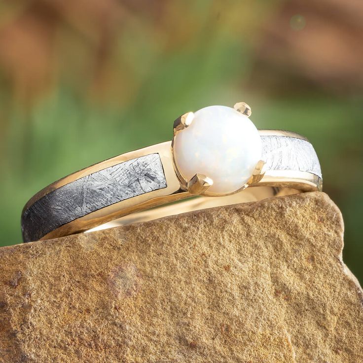 two rings on top of a rock with a white pearl in the middle and black band