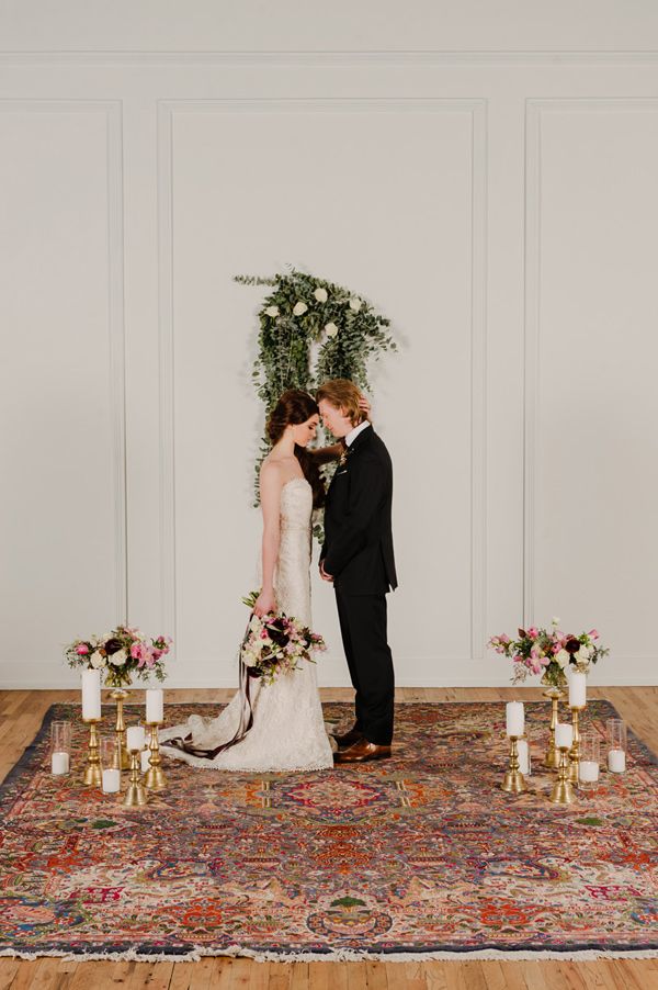 a bride and groom standing in front of a floral arrangement on a rug with candles