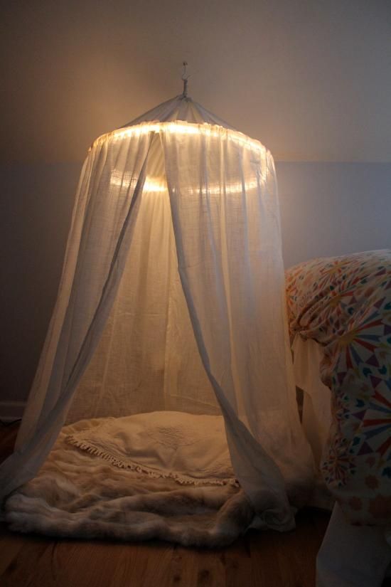 a bed with a white canopy over it in a room next to a pillow on the floor