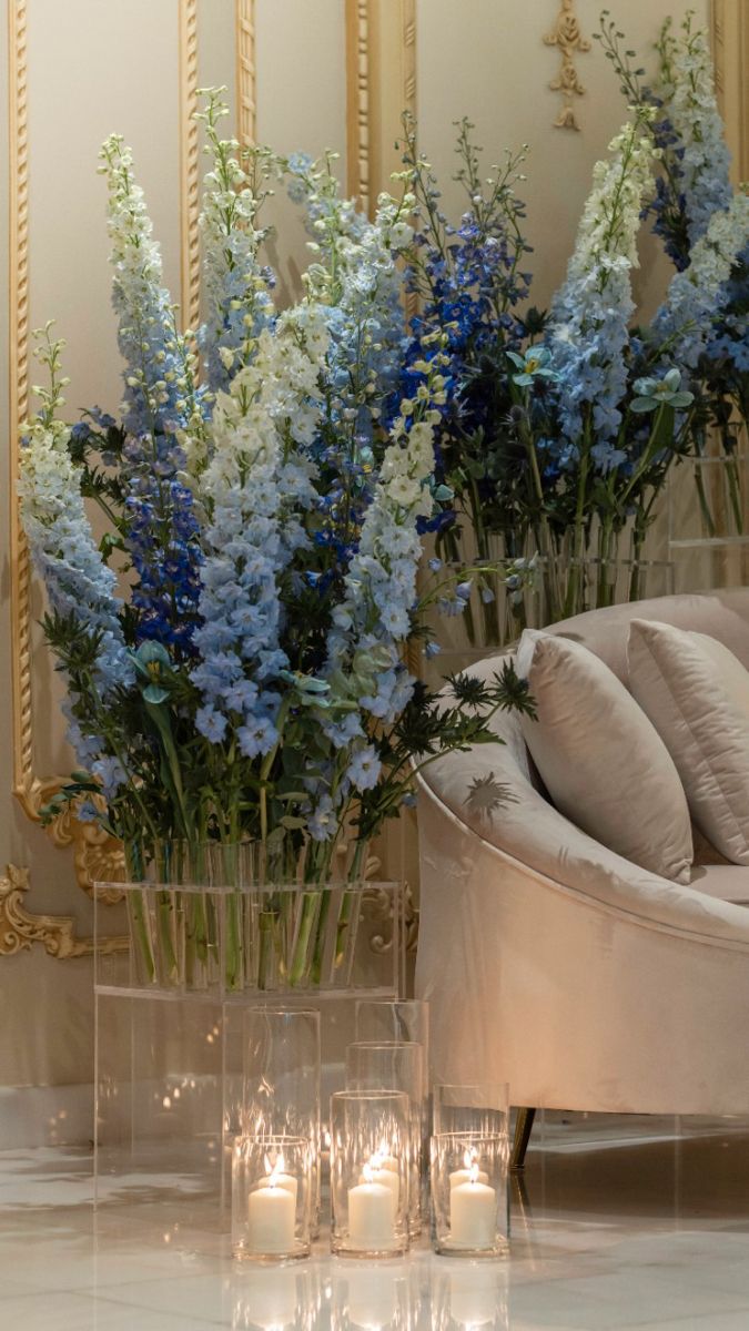 blue and white flowers are in a vase on the floor next to a couch with candles