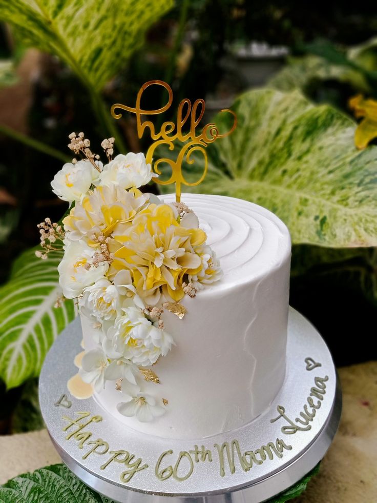 a white cake with yellow flowers on top and the word hello written in gold lettering