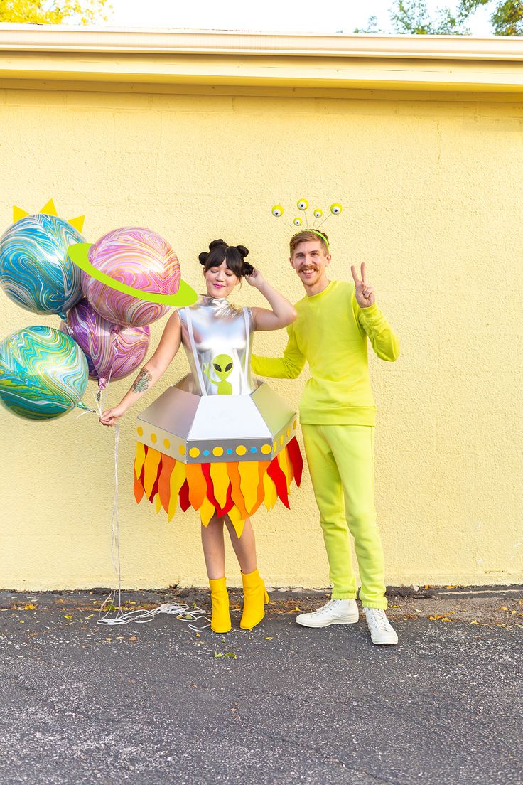 a man and woman in costume standing next to each other near a wall with balloons